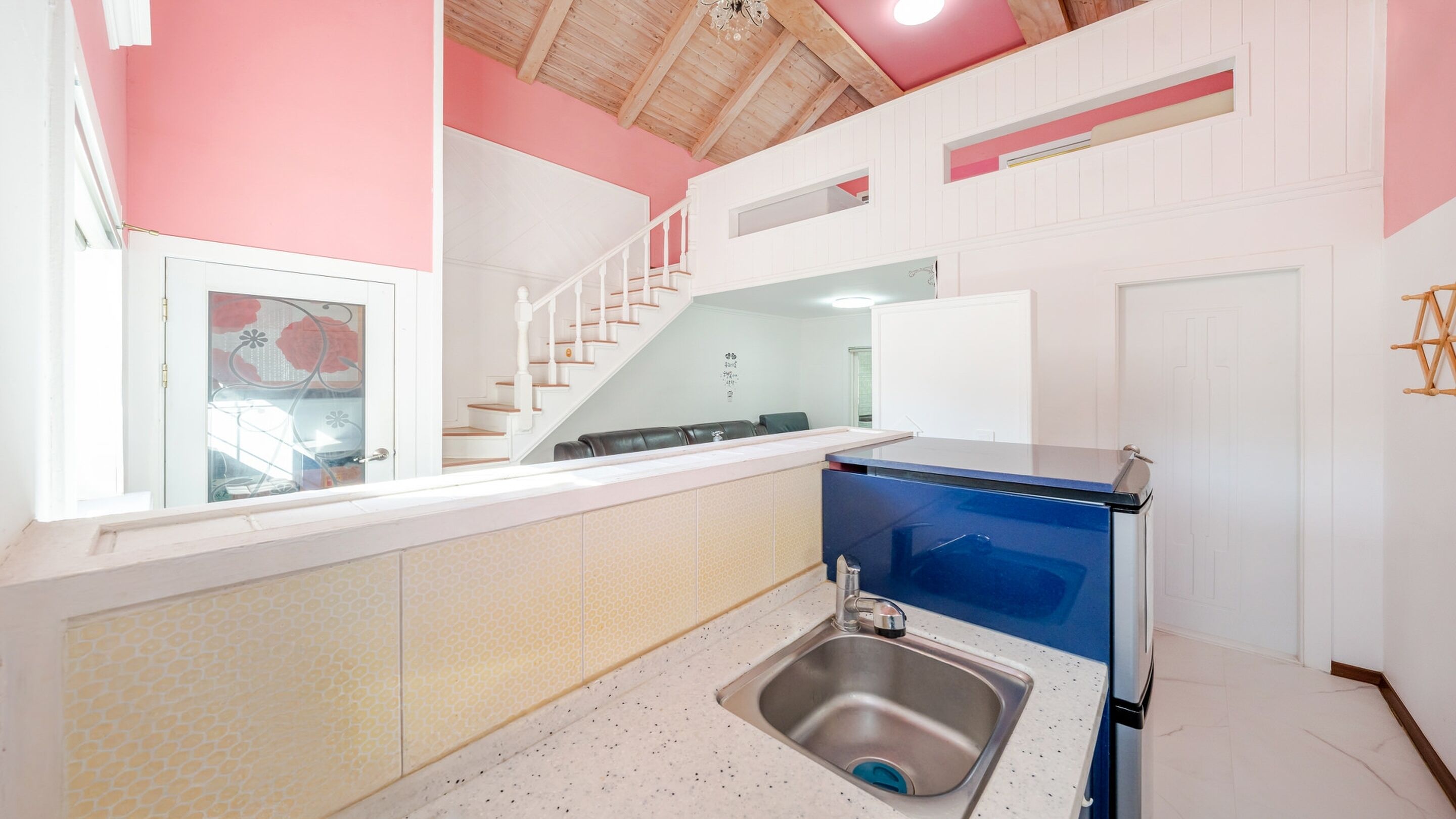 A modern kitchen with a sink, a blue refrigerator, and a staircase leading to an upper level.