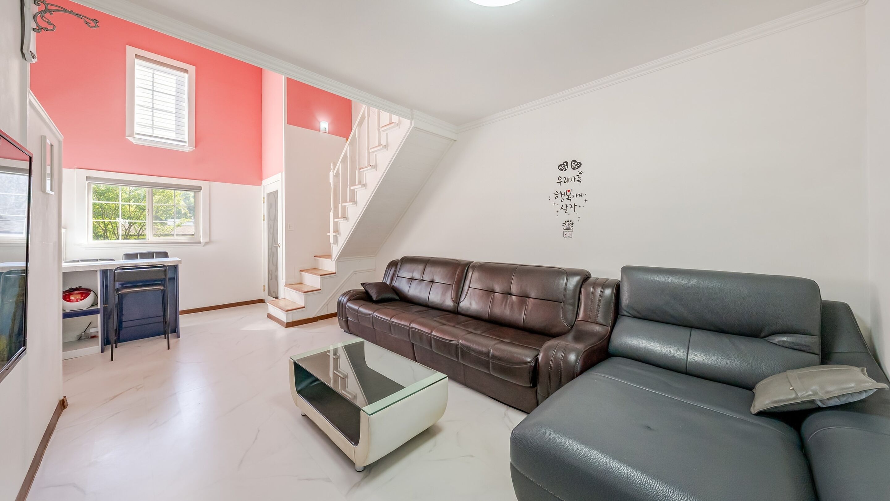 Una sala de estar moderna con un sofá de cuero marrón, una mesa de centro de vidrio y una escalera que conduce a un nivel superior.