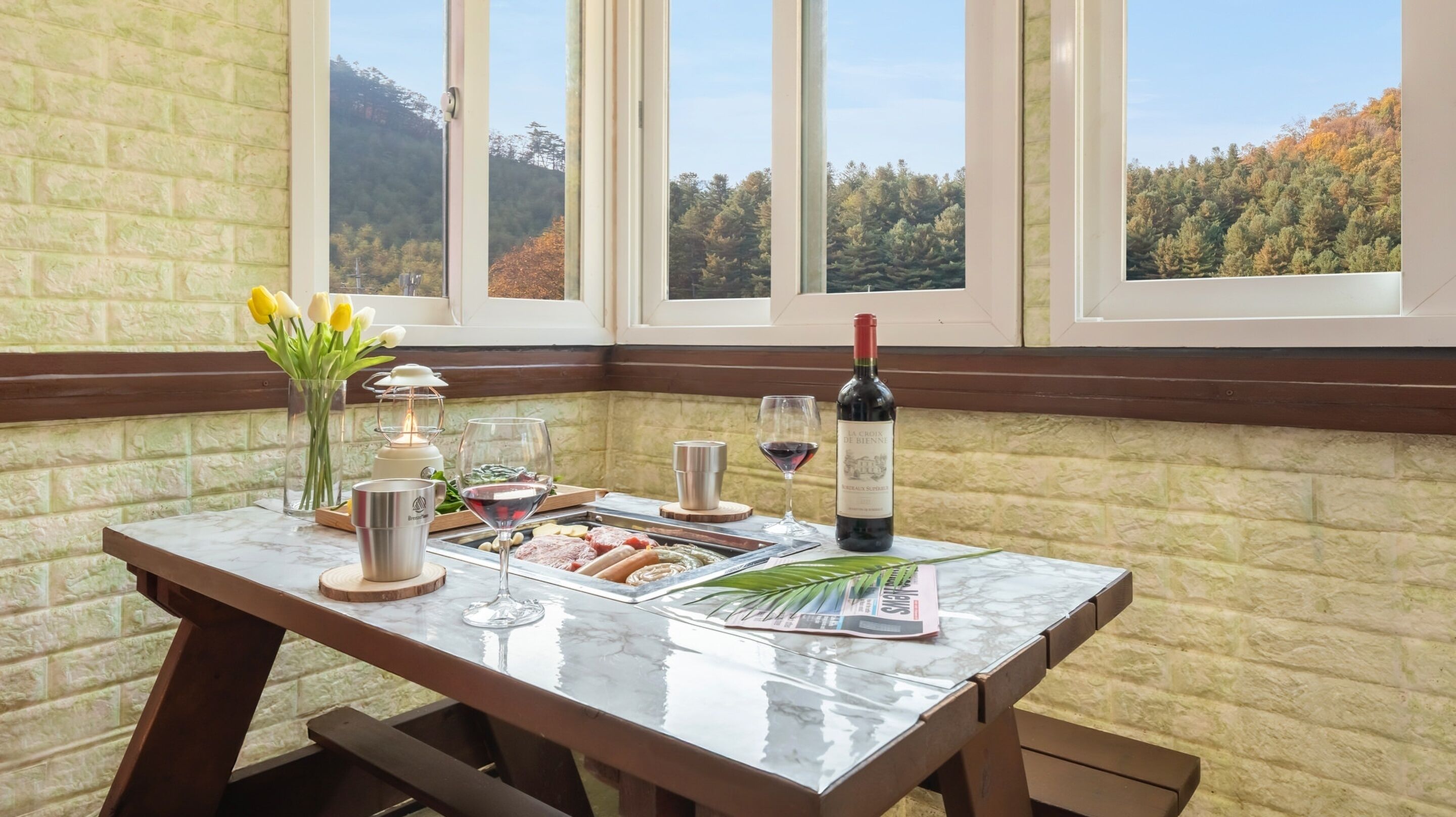 Une table en marbre avec une bouteille de vin, des verres, un plateau de nourriture, une bougie et un vase de fleurs.