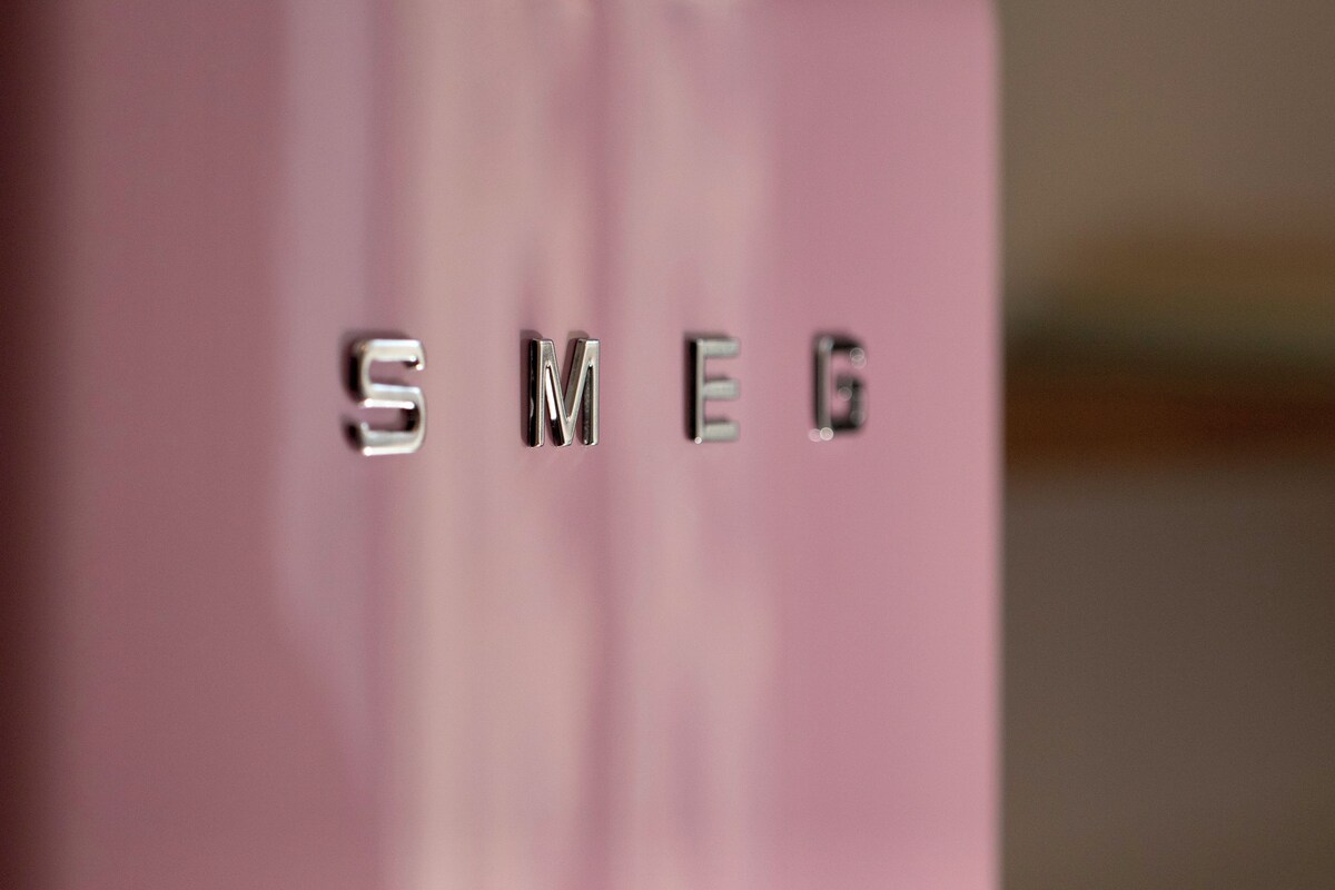 A close-up of metallic letters spelling "SMEG" on a pink surface.
