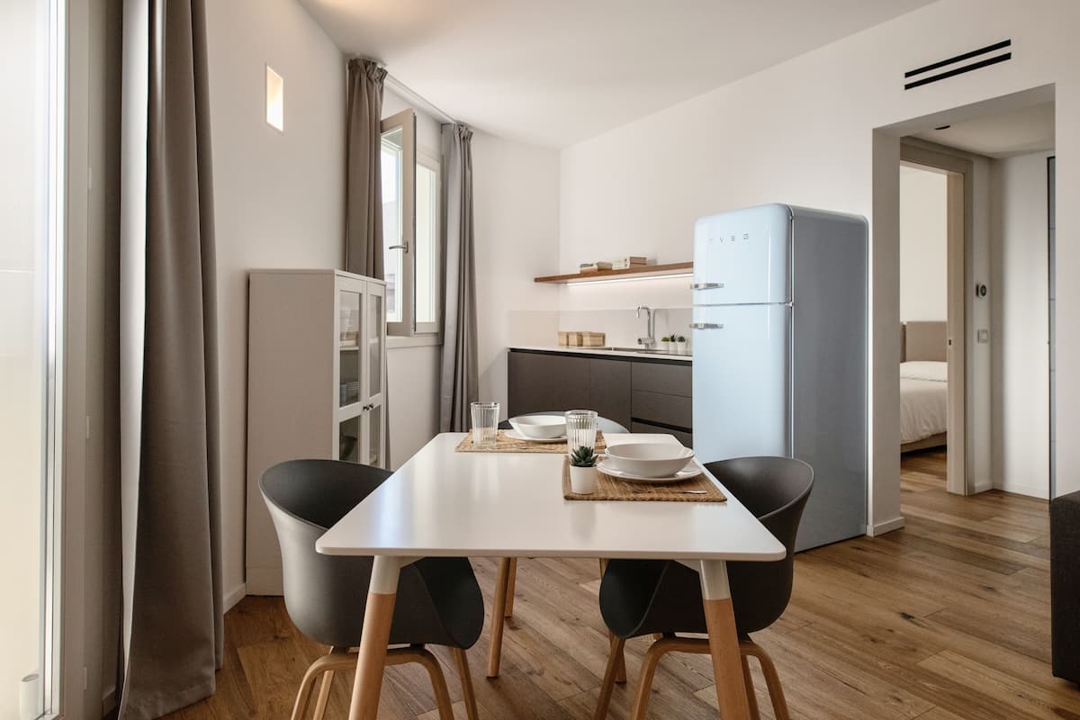 A modern kitchen with a white table, two black chairs, and a blue refrigerator.