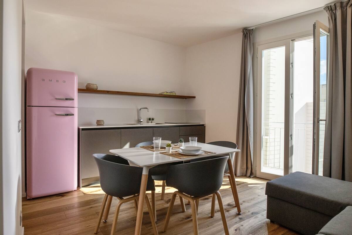 A compact kitchen with a pink refrigerator, a dining table with four chairs, and a small countertop with a sink.