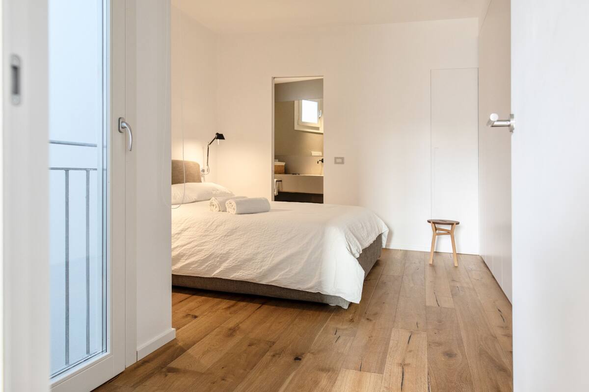 A bedroom with a bed, a nightstand, a lamp, and a wooden stool.