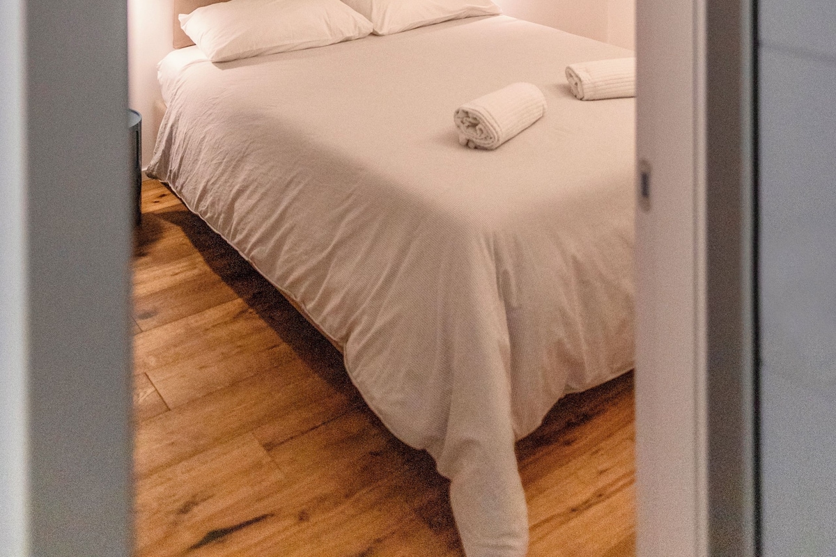 A bedroom with a bed, a nightstand, and a wall-mounted light.