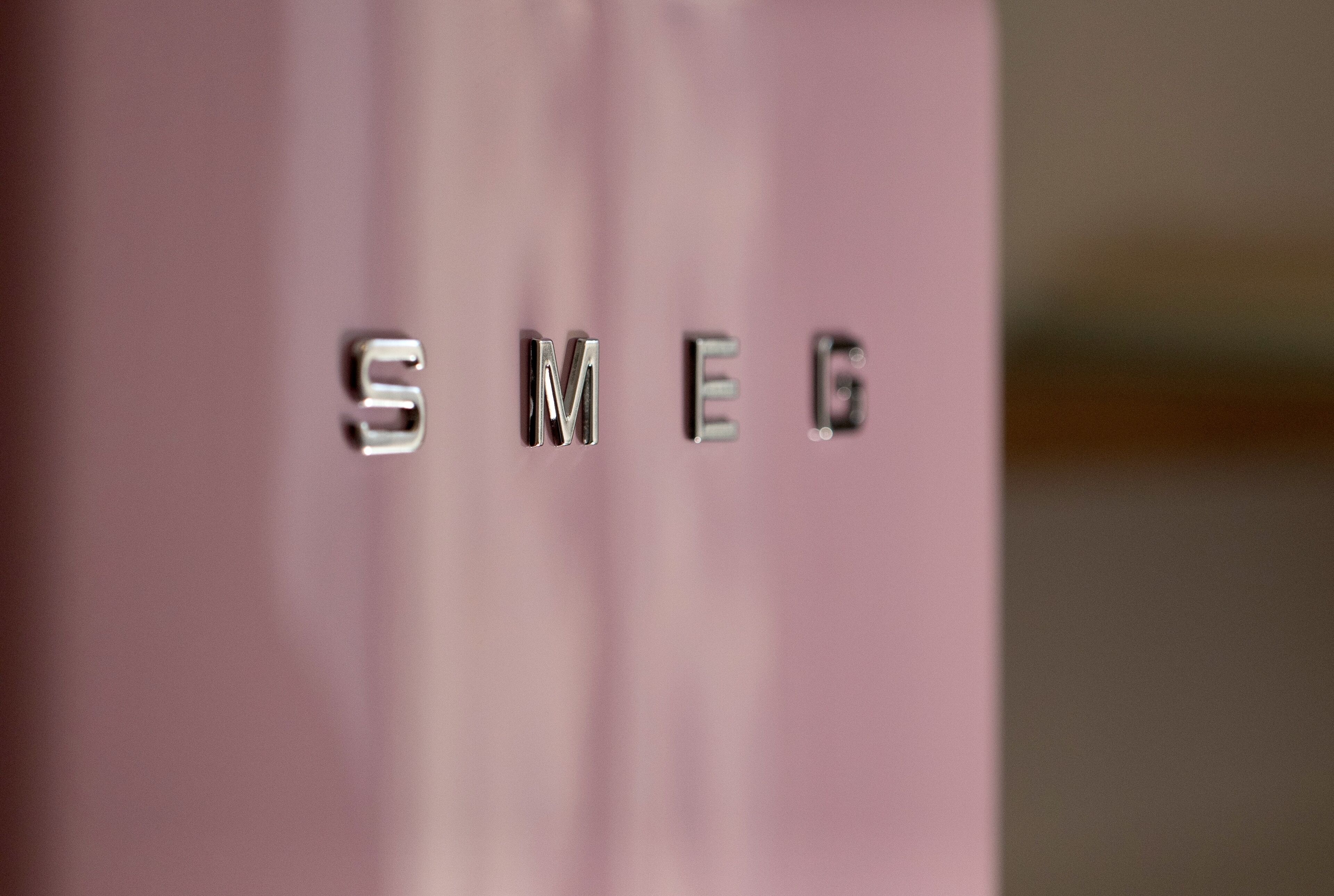A close-up of metallic letters spelling "SMEG" on a pink surface.