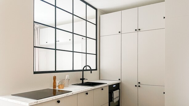 A modern kitchen with a large window, white cabinets, a black sink, and a built-in oven. - Central 1BR next to the park (Helsinki)