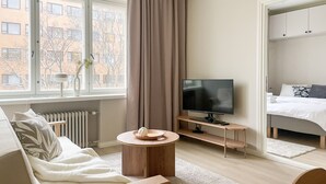 A modern hotel room with a sofa, a TV, a small wooden table, and a bed. - Central 1BR next to the park (Helsinki)
