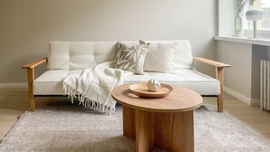 A neutral-toned living room with a sofa, a round wooden coffee table, and a window with a radiator. - Central 1BR next to the park (Helsinki)