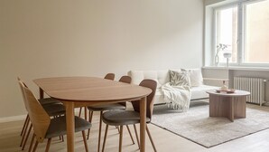 A modern living room with a wooden dining table, chairs, a white sofa, and a small side table. - Central 1BR next to the park (Helsinki)