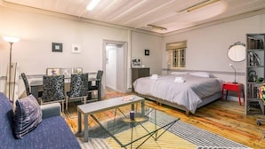A modern hotel room with a bed, a desk with chairs, a small table, and a bookshelf.