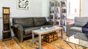 A living room with a leather sofa, a wooden coffee table, a glass coffee table, a bookshelf with books and decorative items, and a clock on a shelf.