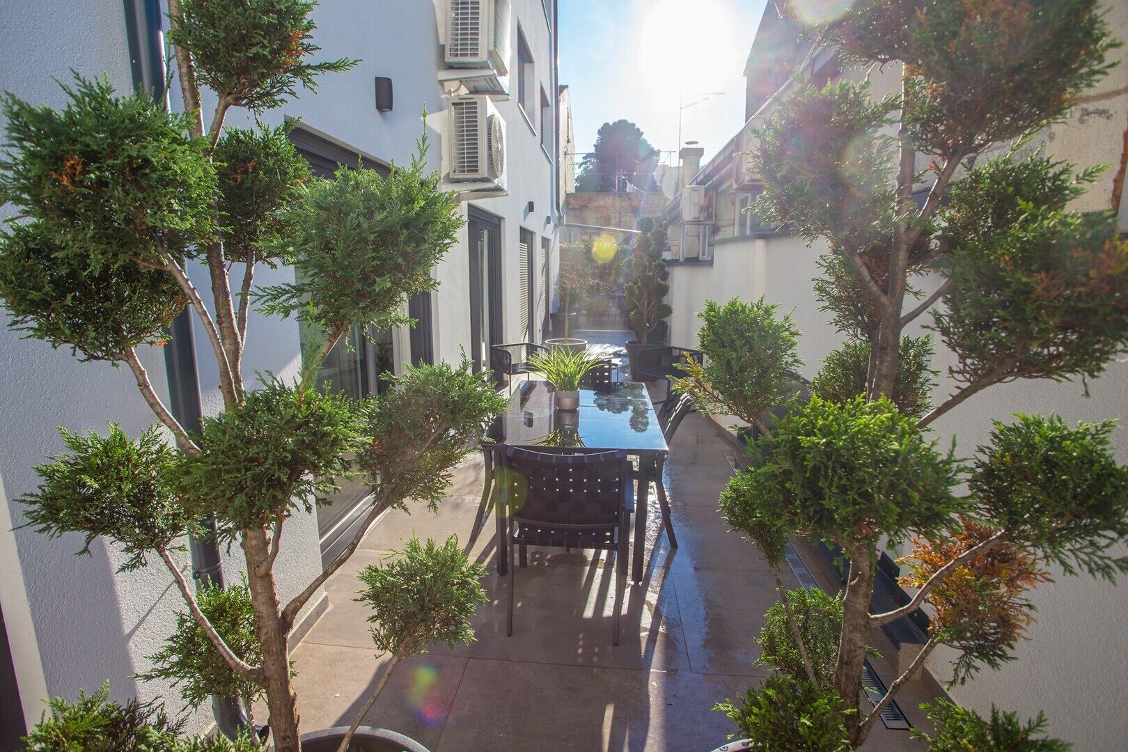 A narrow alleyway with a table and chairs, surrounded by trees and buildings.
