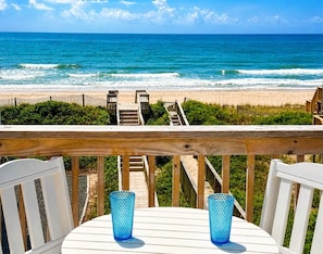 Une terrasse en bois avec une table et des chaises, donnant sur une plage et l’océan.