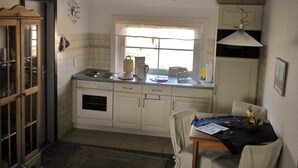 A kitchen with white cabinets, a window, a sink, and a dining table with chairs. - Casa del mar - Casa 2 (Cuxhaven)