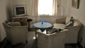 A living room with two armchairs, a small round table, a television, and a window with curtains. - Casa del mar - Casa 2 (Cuxhaven)