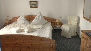 A bedroom with a wooden bed, white bedding, a bedside table with a lamp, a chair, and a framed picture on the wall. - Casa del mar - Casa 2 (Cuxhaven)