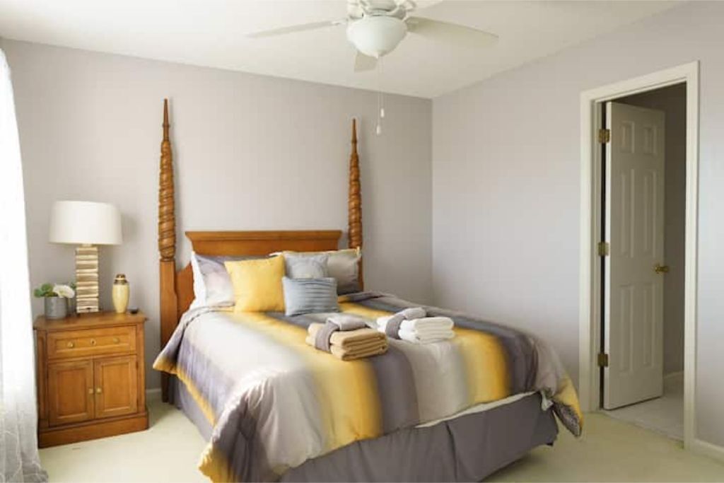 A bedroom with a bed, a nightstand, a lamp, and a door.