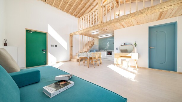 A modern living room with a teal sofa, a dining area with wooden chairs, a kitchen with a blue door, and a staircase with wooden beams. - Gangneung Ggabinejip Hanok Pension (Gangneung)