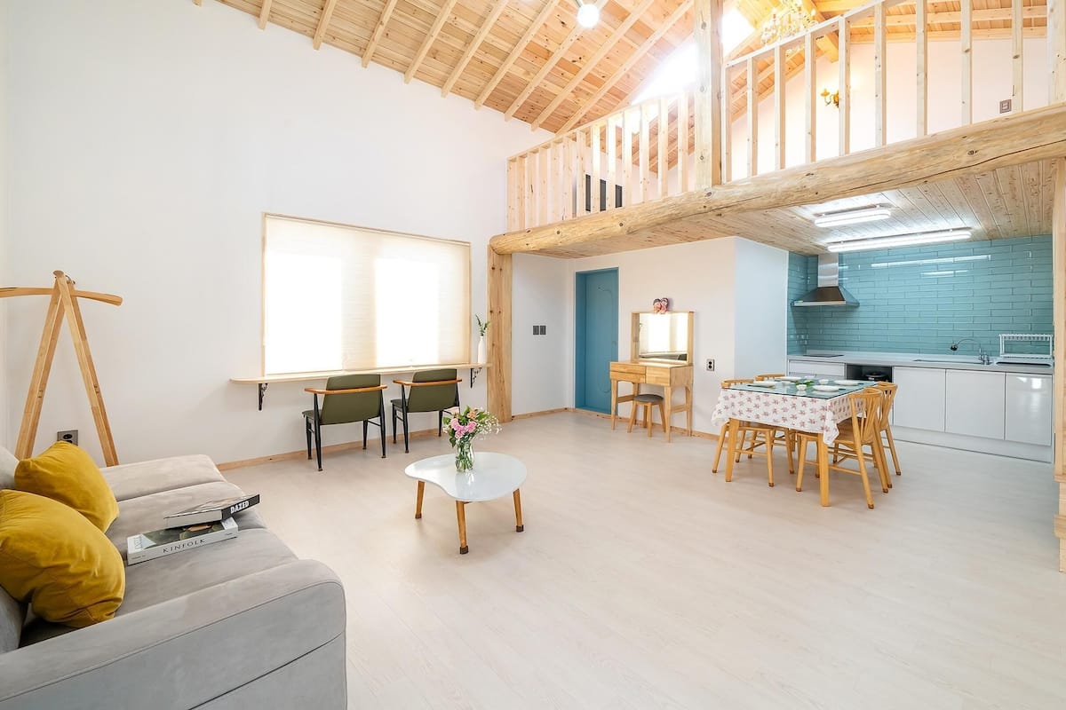 A spacious living area with a loft bedroom, wooden staircase, and a kitchen with blue tiles.
