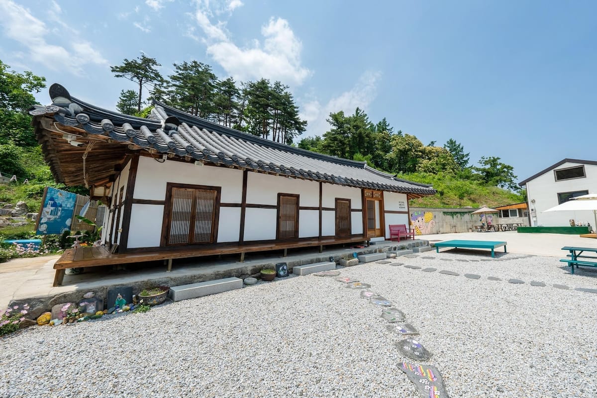 A traditional Japanese building with a tiled roof and wooden beams, a gravel courtyard with benches, and a modern building in the background.
