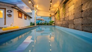 A swimming pool with clear water, surrounded by stone walls and a wooden deck. - Gangneung Ggabinejip Hanok Pension (Gangneung)