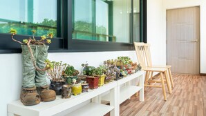 A white bench with various potted plants and a wooden chair on a balcony with a wooden floor and a door in the background. - Gangneung Ggabinejip Hanok Pension (Gangneung)