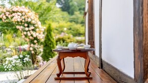 A wooden table with teacups and a teapot on a wooden deck, surrounded by lush greenery and flowers. - Gangneung Ggabinejip Hanok Pension (Gangneung)