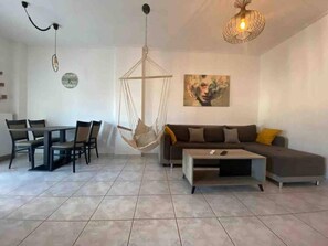 A modern living room with a sofa, coffee table, dining table, chairs, a hanging chair, and a painting on the wall. - Well Designed 2 Bdr Apartment (Ioannina)