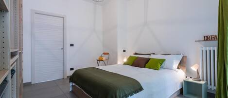 A bedroom with a bed, bedside table, lamp, and a radiator.