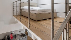 Un dormitorio tipo loft moderno con cama alta, una kitchenette pequeña y una escalera.