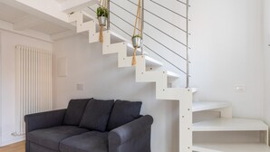 Una sala moderna con un sofá gris, una escalera blanca y un radiador.