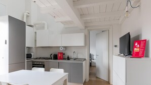 Cocina moderna con armarios blancos, estufa a gas, microondas y un lavamanos. Hay una mesa de comedor con sillas y un televisor sobre un mueble.