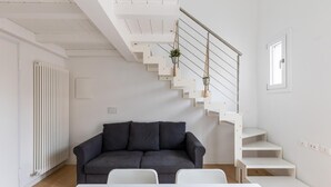 Una sala de estar moderna con un sofá gris, una mesa blanca y una escalera con barandilla blanca y una planta colgante.