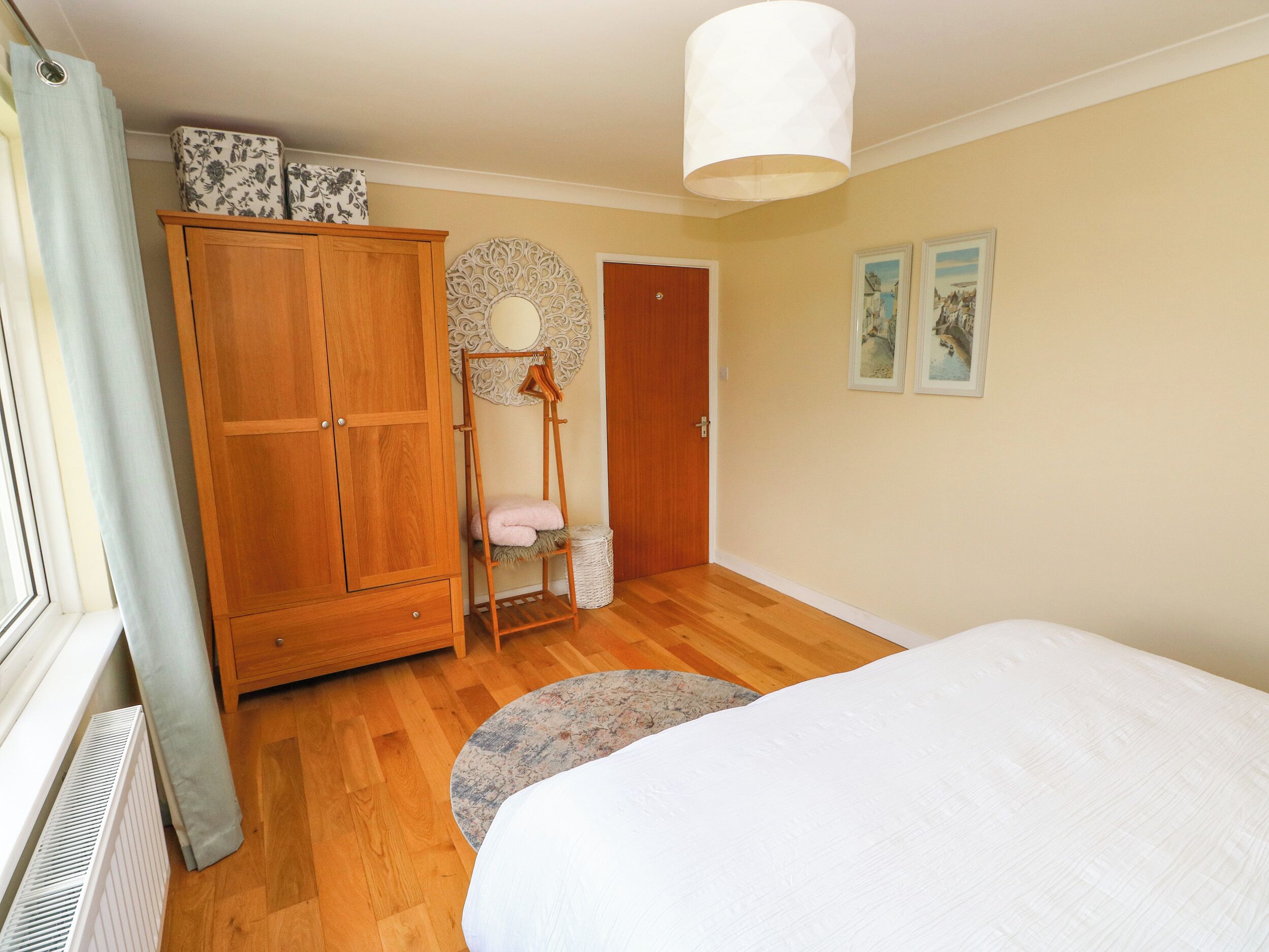 A bedroom with a wooden wardrobe, a round mirror, a bed, and a small rug.
