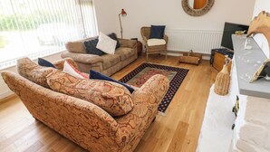 A living room with patterned sofas, a wicker chair, a round mirror, and a wooden table with a vase. - Glynderi (Cardigan)