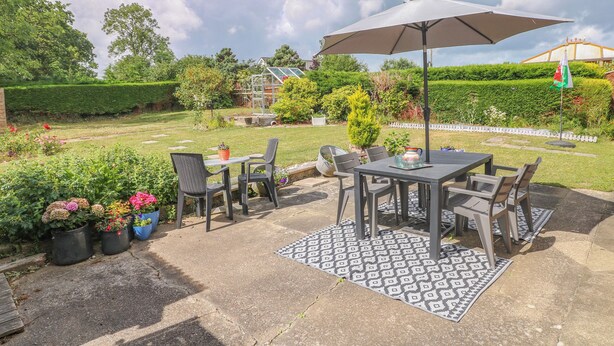 An outdoor patio with a table and chairs, surrounded by potted plants and a patterned rug. - Glynderi (Cardigan)