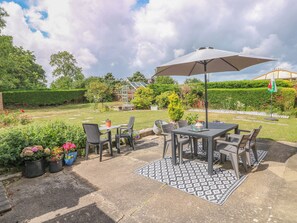 An outdoor patio with a table and chairs, surrounded by potted plants and a patterned rug. - Glynderi (Cardigan)