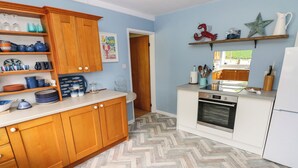 A kitchen with wooden cabinets, a herringbone-patterned floor, and a built-in oven. - Glynderi (Cardigan)
