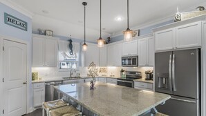 A spacious kitchen with white cabinetry, a large island with bar stools, stainless steel appliances, and pendant lighting.
