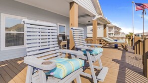 A covered outdoor deck with white lounge chairs and a flag.