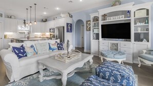 A spacious living room with a white sofa, a coffee table, and a TV in a white entertainment unit.