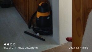 A kitchen with a clock, framed pictures, and a vacuum cleaner.