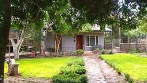 A small house with a stone pathway leading to the entrance, surrounded by a well-maintained garden and trees.