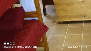 A bedroom with a bed, a wooden bench, a painting on the wall, and a window with curtains.