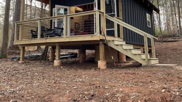 Une cabane dotée d’une terrasse en bois, d’un porche couvert et d’un escalier menant à l’entrée.
