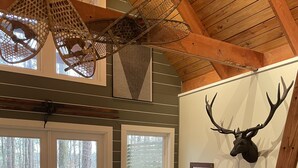 Une chambre avec un grand lit, un plafond en bois, une tête de cerf accrochée au mur et une vue sur l’extérieur grâce à une porte coulissante.