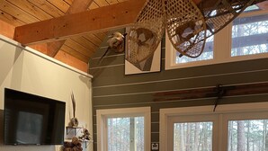 Un salon confortable avec un canapé, une table basse et un téléviseur. Il y a deux fenêtres donnant sur des arbres et une terrasse à l’extérieur.