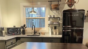 Une cuisine moderne avec une table en bois foncé, deux tabourets assortis, un réfrigérateur noir et une fenêtre donnant sur des arbres.