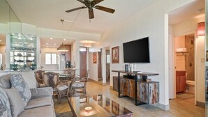A spacious living area with a sofa, dining table, and chairs, a television, and a kitchen area with cabinets and a countertop. - Menehune Shores, #623 2 Bedroom Condo by RedAwning (Kihei)