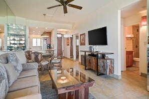 A spacious living area with a sofa, dining table, and chairs, a television, and a kitchen area with cabinets and a countertop.